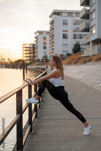 Beautiful woman in sport suit for fitness makes stretching exercises on the street. Young girl practicing sports outdoors. Concept of healthy lifestyle, sport, urban life