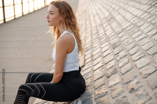 Caucasian woman in sport suit for fitness relaxing after exercises on the street. Concept of healthy lifestyle, sport, urban life