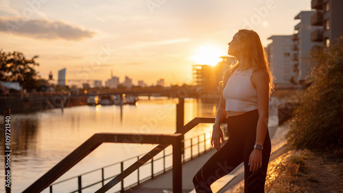 Caucasian woman in sport clothes for fitness relaxing after exercises on the street during the sunset. Concept of healthy lifestyle, sport, urban life