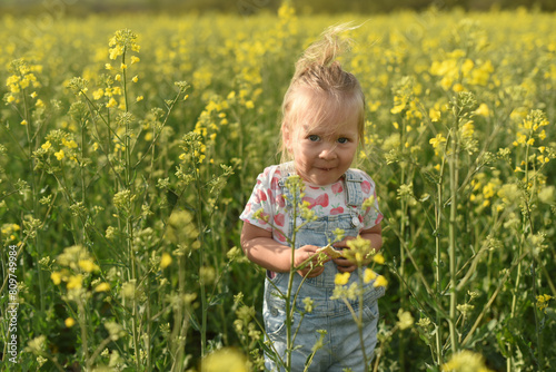 A little girl of two years old is walking in a field. A child walks in a rapeseed field. Blonde little girl of two years old