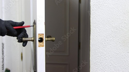 A hand with black latex gloves and a red screwdriver fixing the lock of an interior door. Isolated on a white background. Spare parts and maintenance. photo