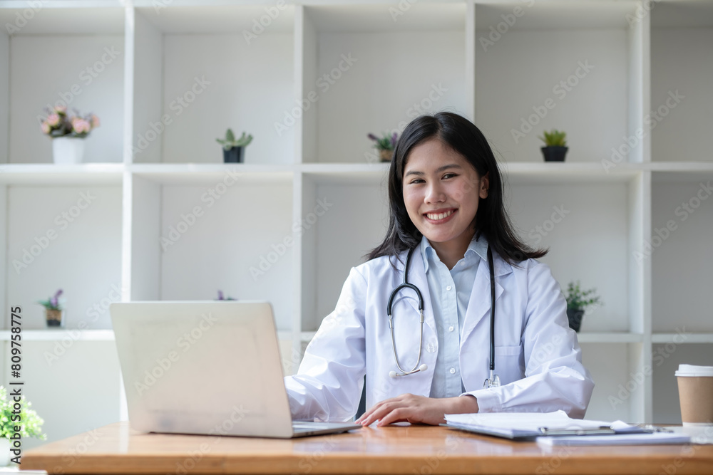 young asian lady doctor in white medical uniform with stethoscope using computer laptop talking video conference call with patient at desk in health clinic or hospital. young asian lady doctor in white medical uniform with stethoscope using computer laptop talking video conference call with patient at desk in health clinic or hospital.