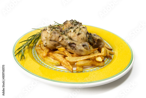 Garlic chicken thighs with French fries, served on a yellow plate, with a sprig of rosemary. Isolated on a white background. Spanish food concept.