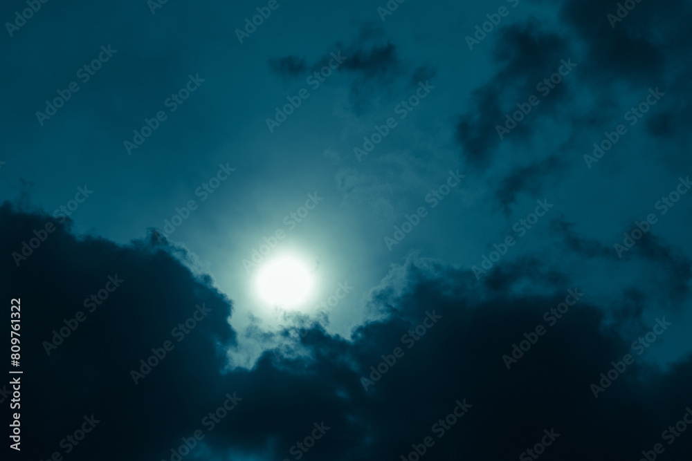 Cloudy night sky with shining full moon through the dark clouds.