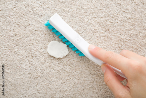 Foto Young adult woman hand holding brush and removing chewing gum from light beige home carpet