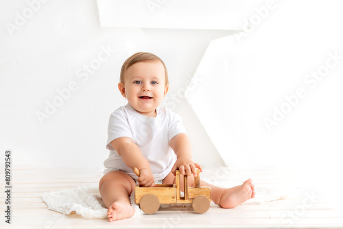 a small child is sitting with a wooden toy car on a white isolated background, a baby is playing at home in a white T-shirt, a place for text