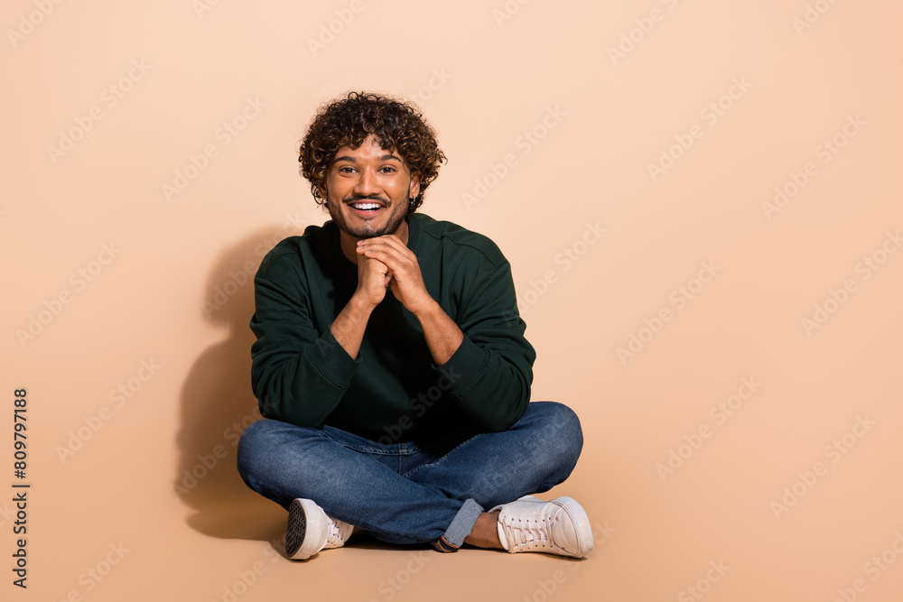 Full size photo of nice young man sit floor empty space wear sweater isolated on beige color background