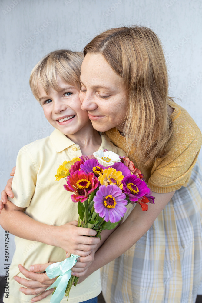mom hugs her son holding flowers. Mother's Day concept. Family portrait of a cute 6 year old boy and woman. birthday. The atmosphere of family love and positivity. Happy motherhood mom hugs her son holding flowers. Mother's Day concept. Family portrait of a cute 6 year old boy and woman. birthday. The atmosphere of family love and positivity. Happy motherhood