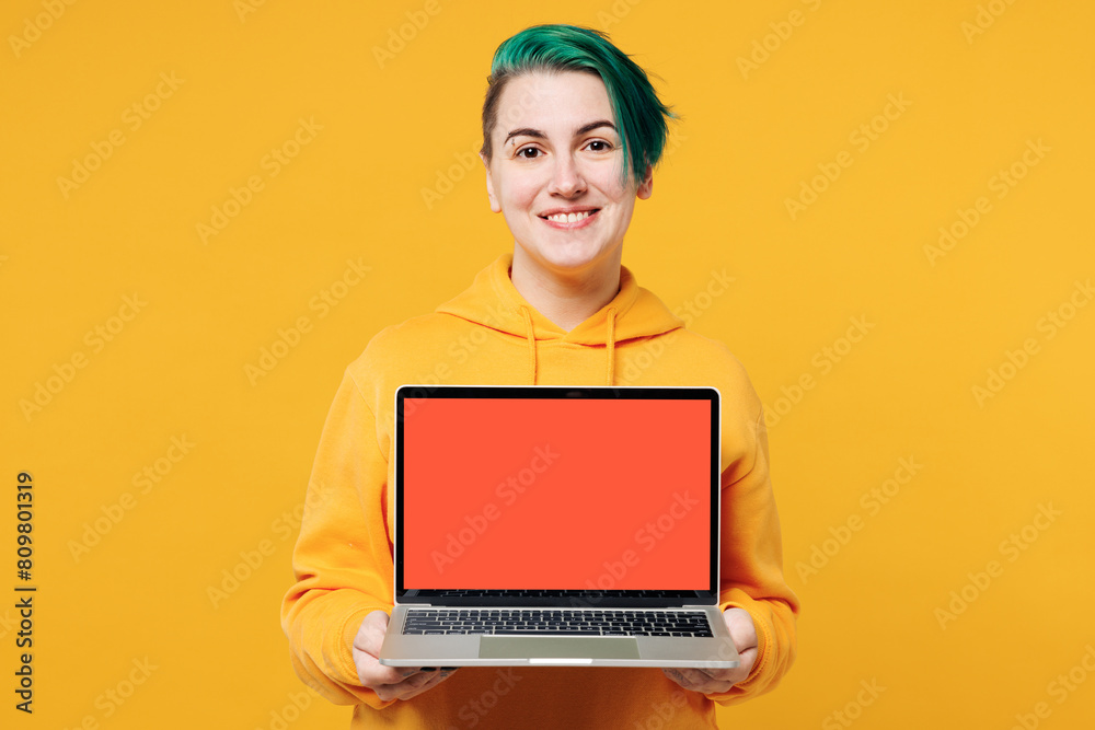 Young happy IT woman with dyed green hair wear hoody casual clothes hold use work on blank screen workspace area laptop pc computer isolated on plain yellow orange background studio Lifestyle concept Young happy IT woman with dyed green hair wear hoody casual clothes hold use work on blank screen workspace area laptop pc computer isolated on plain yellow orange background studio Lifestyle concept