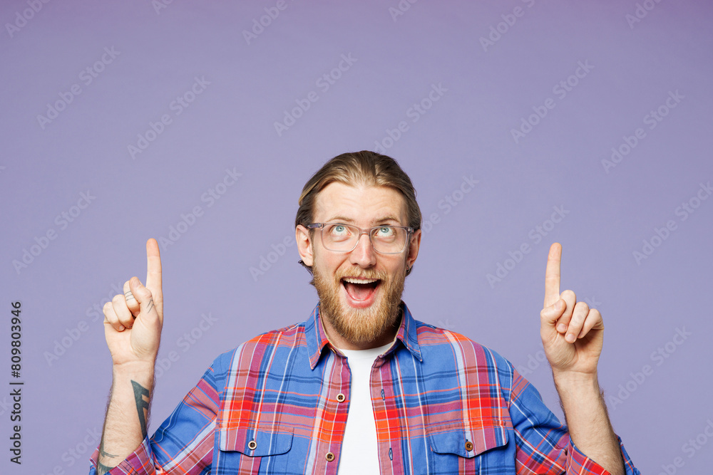 Young surprised happy man wears blue shirt casual clothes point index finger overhead indicate on workspace area copy space mock up isolated on plain pastel light purple background. Lifestyle concept. Young surprised happy man wears blue shirt casual clothes point index finger overhead indicate on workspace area copy space mock up isolated on plain pastel light purple background. Lifestyle concept.