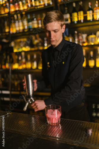 Bartender prepares metal siphon to add whipped cream to glamorous pink cocktail standing on bar counter. Barman makes nonalcoholic creamy beverage