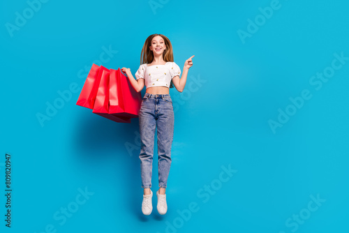 Full length portrait of lovely girl jump direct finger empty space wear top isolated on blue color background