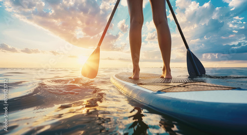 Close up of a woman's legs on a paddleboard in the ocean, a closeup view of someone standup paddleboarding with a beautiful blue sky and calm sea water. photo