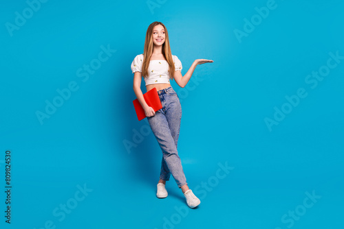 Photo of positive happy girl hold hand demonstrate empty space isolated blue color background
