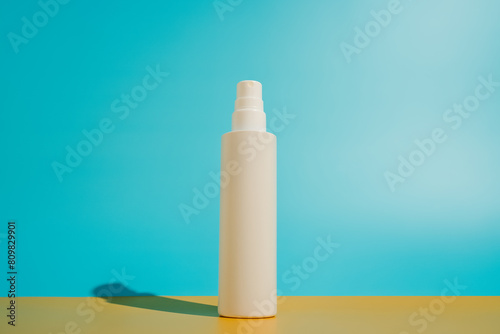 Blank white spray bottle on yellow and blue background in direct sunlight. Summer skin protection mockup template with minimalist beach aesthetic photo