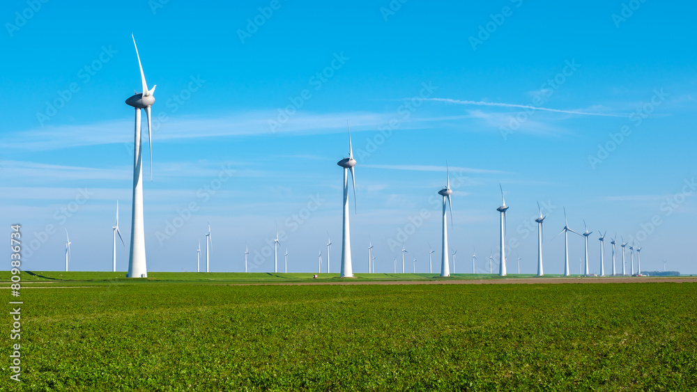 A symphony of wind turbines standing tall in a lush green field in the Netherlands, Flevoland A symphony of wind turbines standing tall in a lush green field in the Netherlands, Flevoland