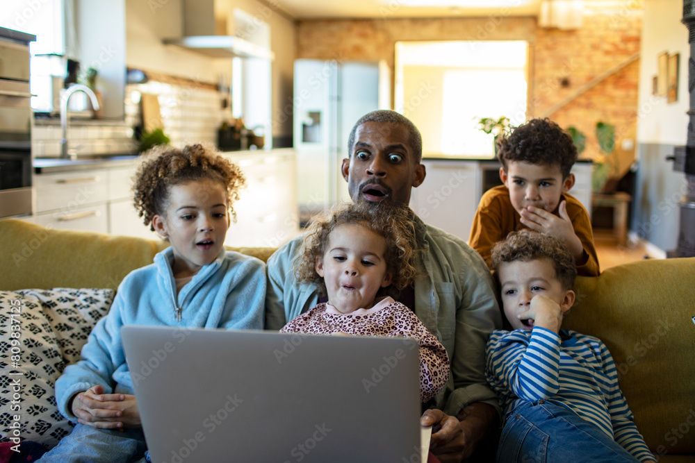 Father using the laptop with his kids on the couch at home Father using the laptop with his kids on the couch at home