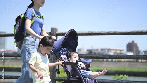 晴天の川沿いの公園でベビーカーで散歩するママと兄弟の親子(3人家族)の上半身　春夏のお出かけやママの通勤などのイメージのスロー動画