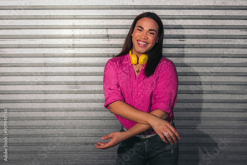 Portrait of trans woman with pink shirt and yellow headphones over gray background.. LGBT people.