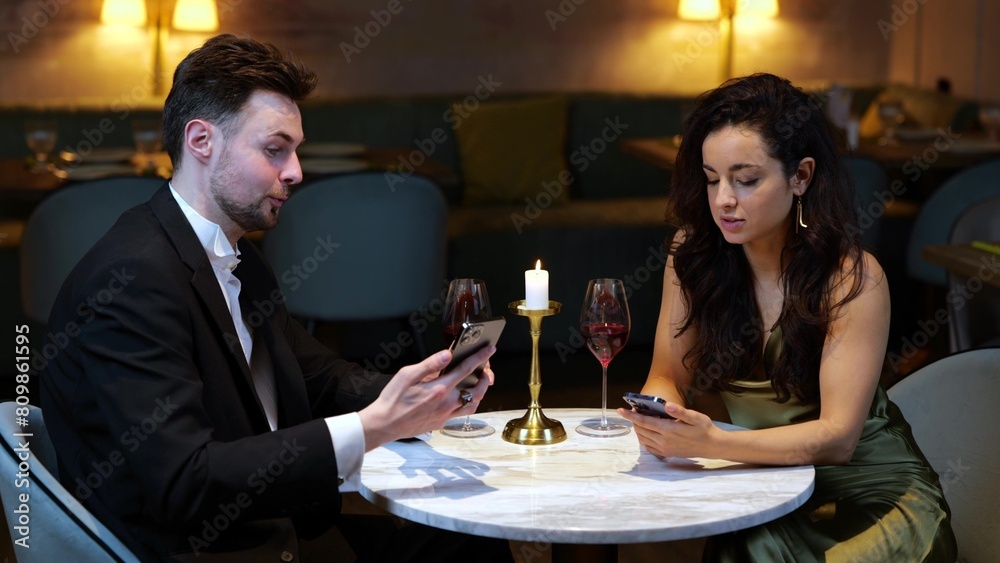 Happy man and woman looking at smartphone screen while sitting in the restaurant, having date. Lifestyle, love, relationships concept. 