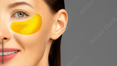 Close-up of a woman with a yellow golden hydrogel under-eye patch on her left cheek, showcasing her glowing skin and subtle makeup.