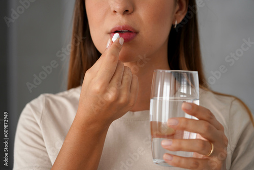Young woman takes a pill while holding a glass of water in her hand
