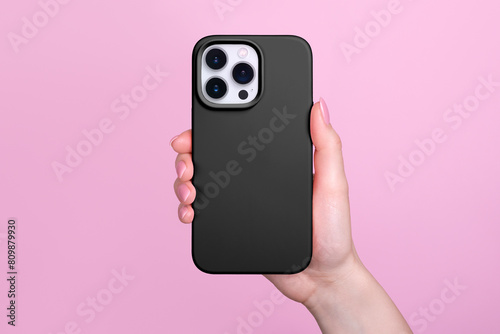 Smartphone in female hand in black silicone cover isolated on pink background phone case mock up in monochrome colours back view