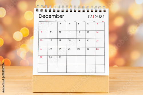 December 2024 desk calendar on wooden table with gold light bokeh background. photo