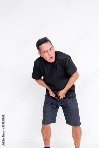 Urgency depicted as a middle-aged Asian man unbuckles his belt, showing signs of low pain tolerance and an immediate need to urinate. photo