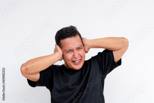 Middle-aged Asian man cringing and covering ears to block noise, isolated on white