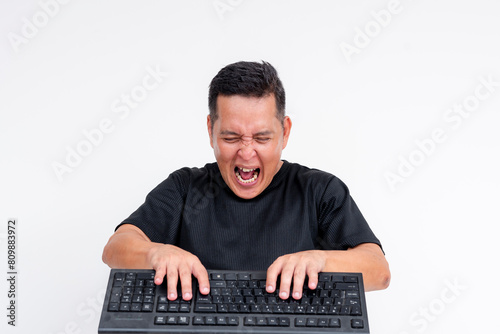A middle aged man is mad and livid while typing furiously on his keyboard. Toxic online behavior or keyboard warrior concepts.