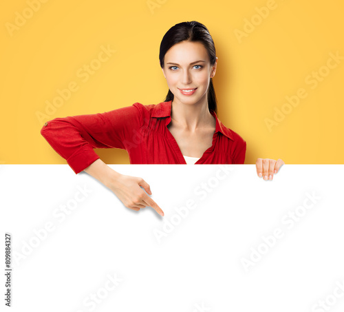 Brunette beautiful woman wear orange casual shirt stand behind, peep from blank empty banner mockup sign board signboard advertise show pointing area for sales slogan text, isolated yellow background.