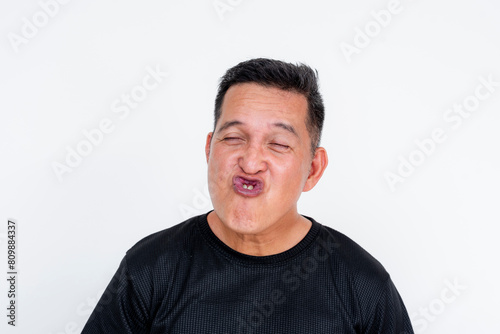 A funny expressive portrait of an Asian man isolated on a white background, puckering lips and squinting eyes.
