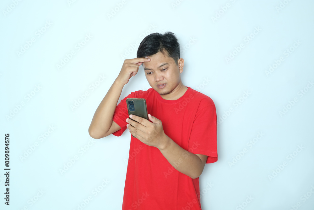 Asian man showing sad expression looking at smartphone. Wearing red t-shirt Asian man showing sad expression looking at smartphone. Wearing red t-shirt