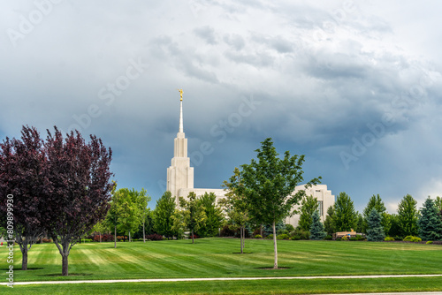 A church building, a temple with a tall spire stand in the background of a mowed field of grass and a grove of trees, Twin Falls, Idaho photo