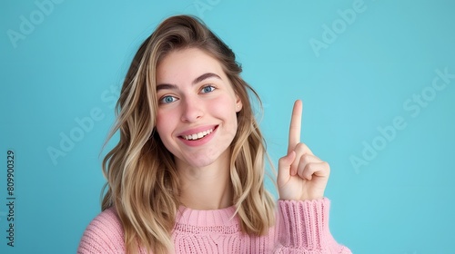 Young cute woman raises index finger, smiles, relaxes, looks at camera , please remember concept