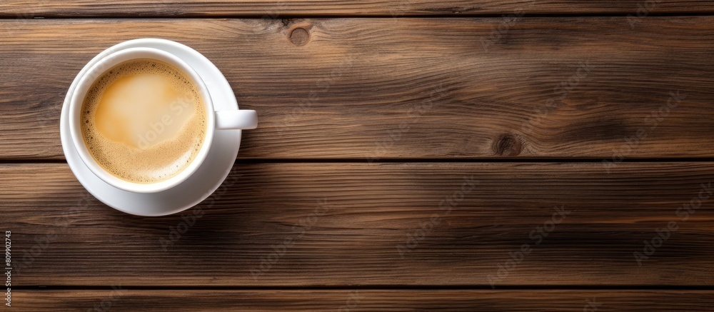 A copy space image of a black coffee cup with milk is seen from a top view on a wooden table background It represents the concept of a morning breakfast drink A copy space image of a black coffee cup with milk is seen from a top view on a wooden table background It represents the concept of a morning breakfast drink