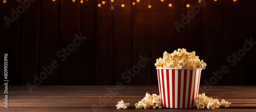 There is a bucket of popcorn placed on a wooden table inside a cinema hall The table has empty space available for text or any other information. Creative banner. Copyspace image