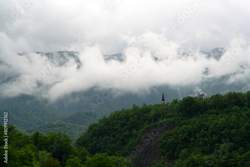 Clouds over the tops of mountains with green slopes. Church on top of the mountain. Beauty of nature concept background