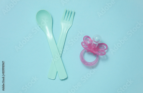 Plastic fork and spoon  pacifier for baby on a blue background. Top view