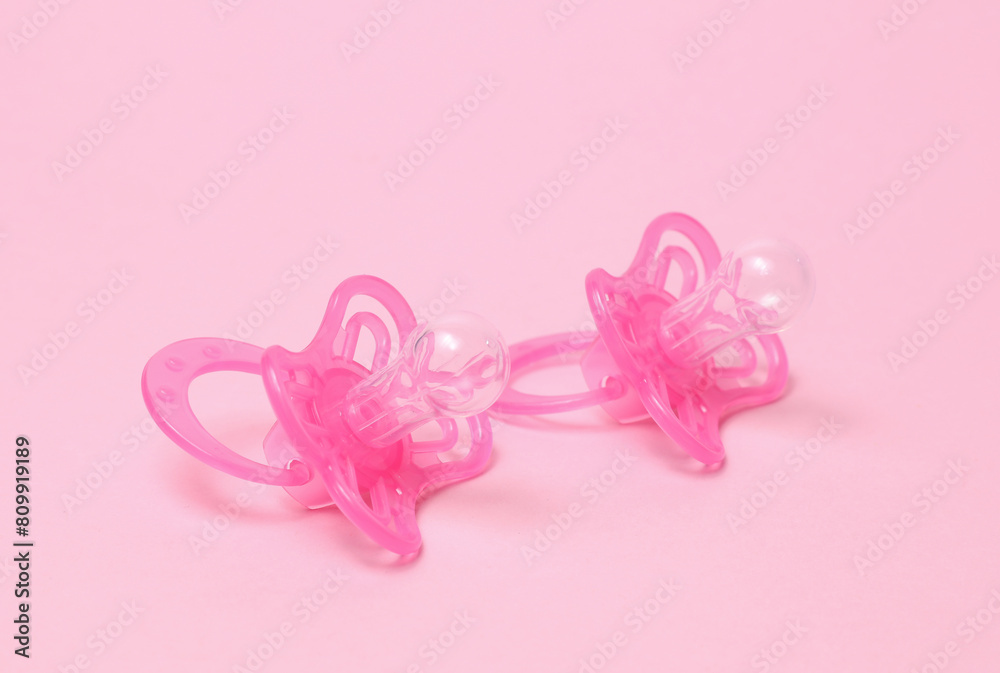 Two baby pacifiers on pink background.