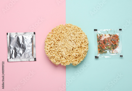 Dry instant noodles with spice packets on pink blue background. Top view