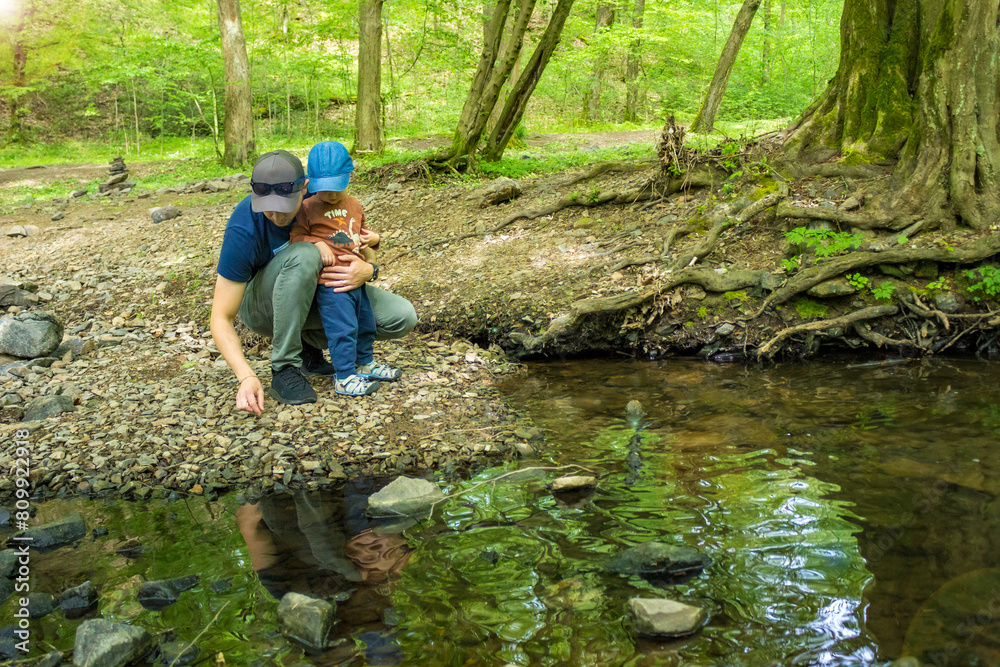 Dad with son toddler hiking together at sping forest near the river. Dad with son toddler hiking together at sping forest near the river.