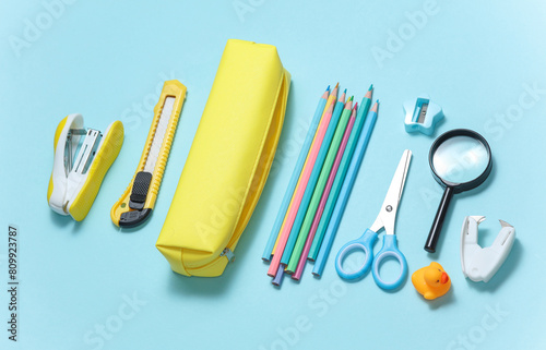 Yellow school pencil case with stationery and school accessories on a blue background. Back to school concept. Top view. Flat lay