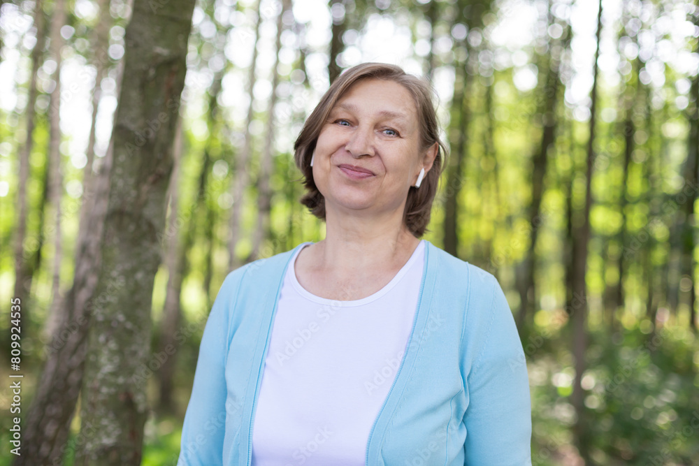 Beautiful smiling mature woman with wireless headphones walking in nature. Healthy lifestyle concept Beautiful smiling mature woman with wireless headphones walking in nature. Healthy lifestyle concept