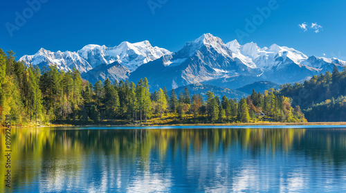 A majestic mountain range with snow-capped peaks, clear blue skies and a calm lake in the foreground.