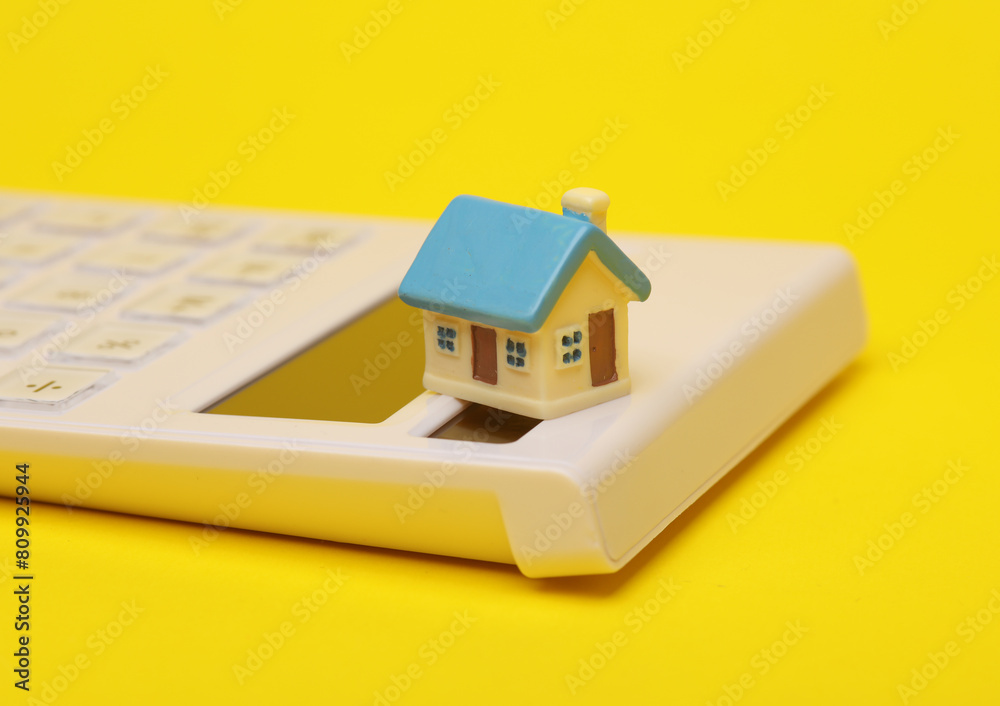 CAlculator with a house miniature on a yellow background CAlculator with a house miniature on a yellow background