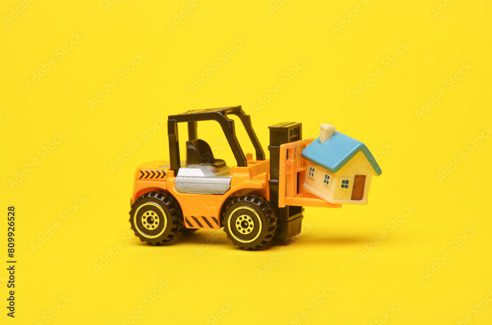 Forklift miniature with house model on yellow background Forklift miniature with house model on yellow background