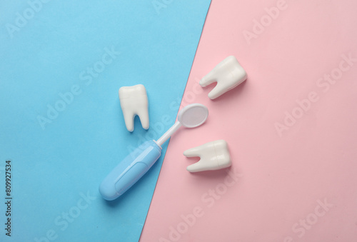 Visit to the dentist, taking care of the oral cavity concept. Toy dental mirror and teeth models on blue pink background