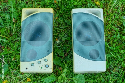 two old small plastic ones with speakers, powerful gray desktop speakers for a computer lie on the green grass outdoors during the day